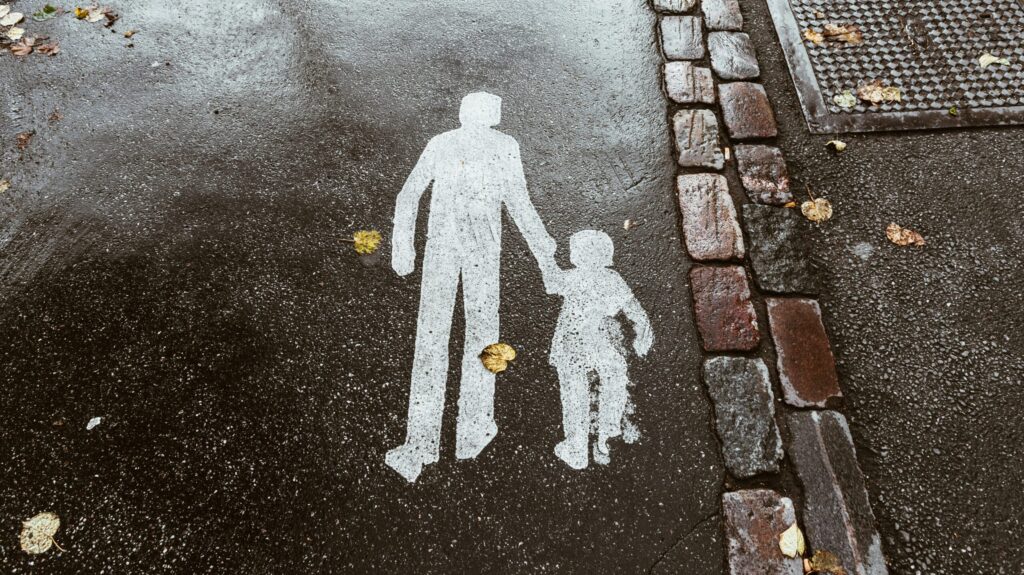 A silhouette painting on a street of an adult holding a child's hand.