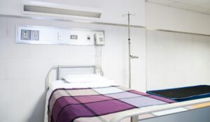 An empty bed in a hospital room with a purple and grey checked blanket.