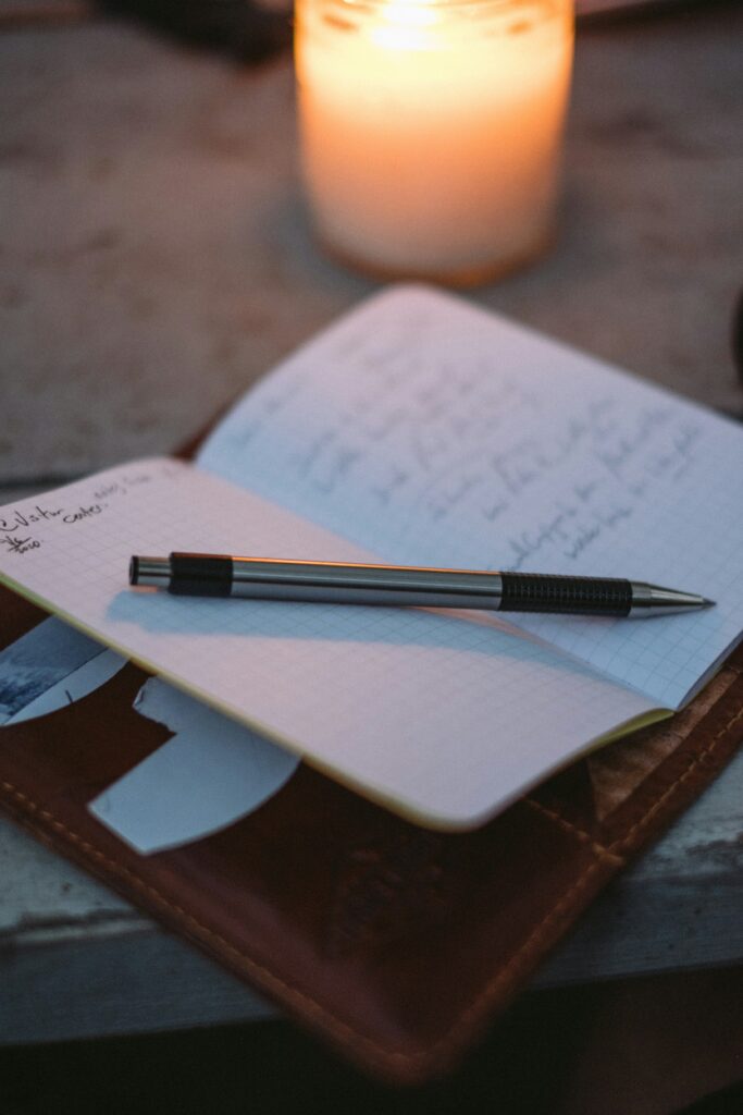 A notebook with handwriting sits in front of a candle.