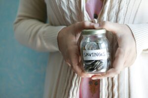 A person holds a jar full of change labeled "savings."