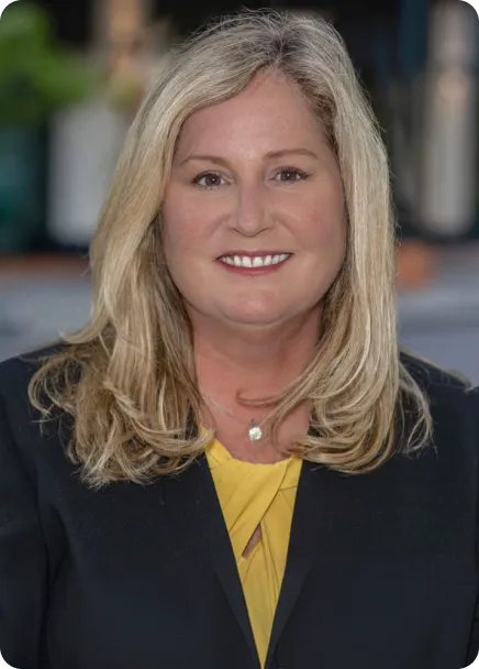Professional portrait of a smiling woman with blonde hair, black blazer, and yellow blouse.