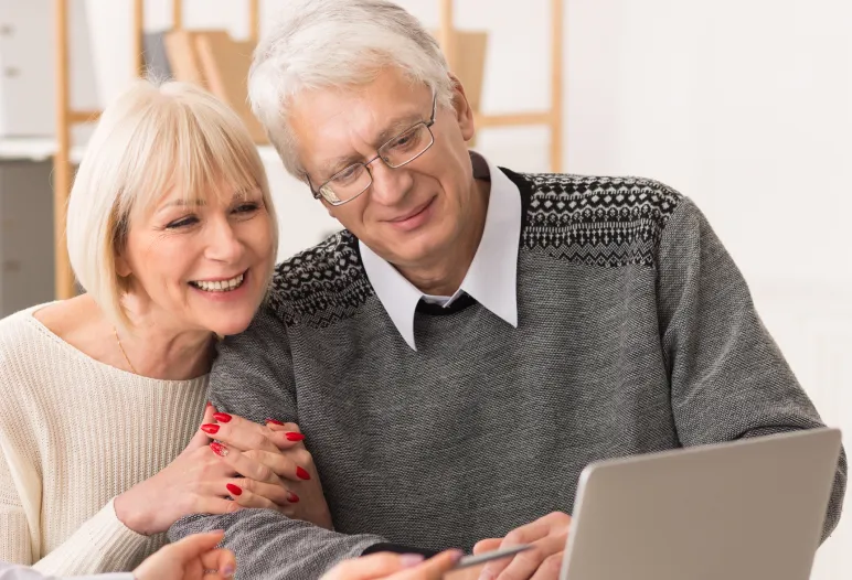 Elderly couple smiling and looking at a laptop screen together indoors.