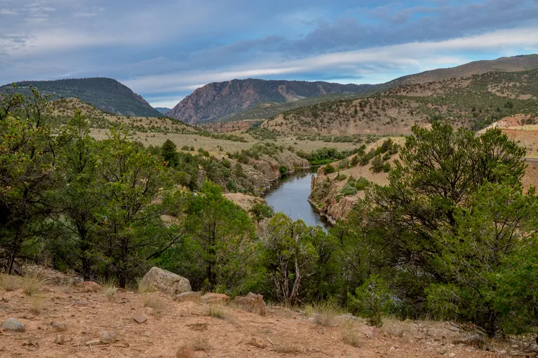 Scenic view of a winding river through green and rocky hills under a cloudy sky.