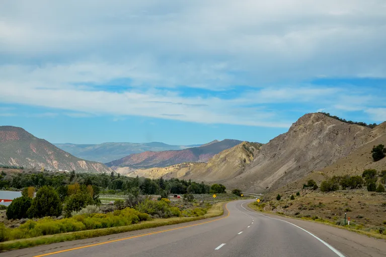Scenic highway curving through mountainous landscape under partly cloudy sky.