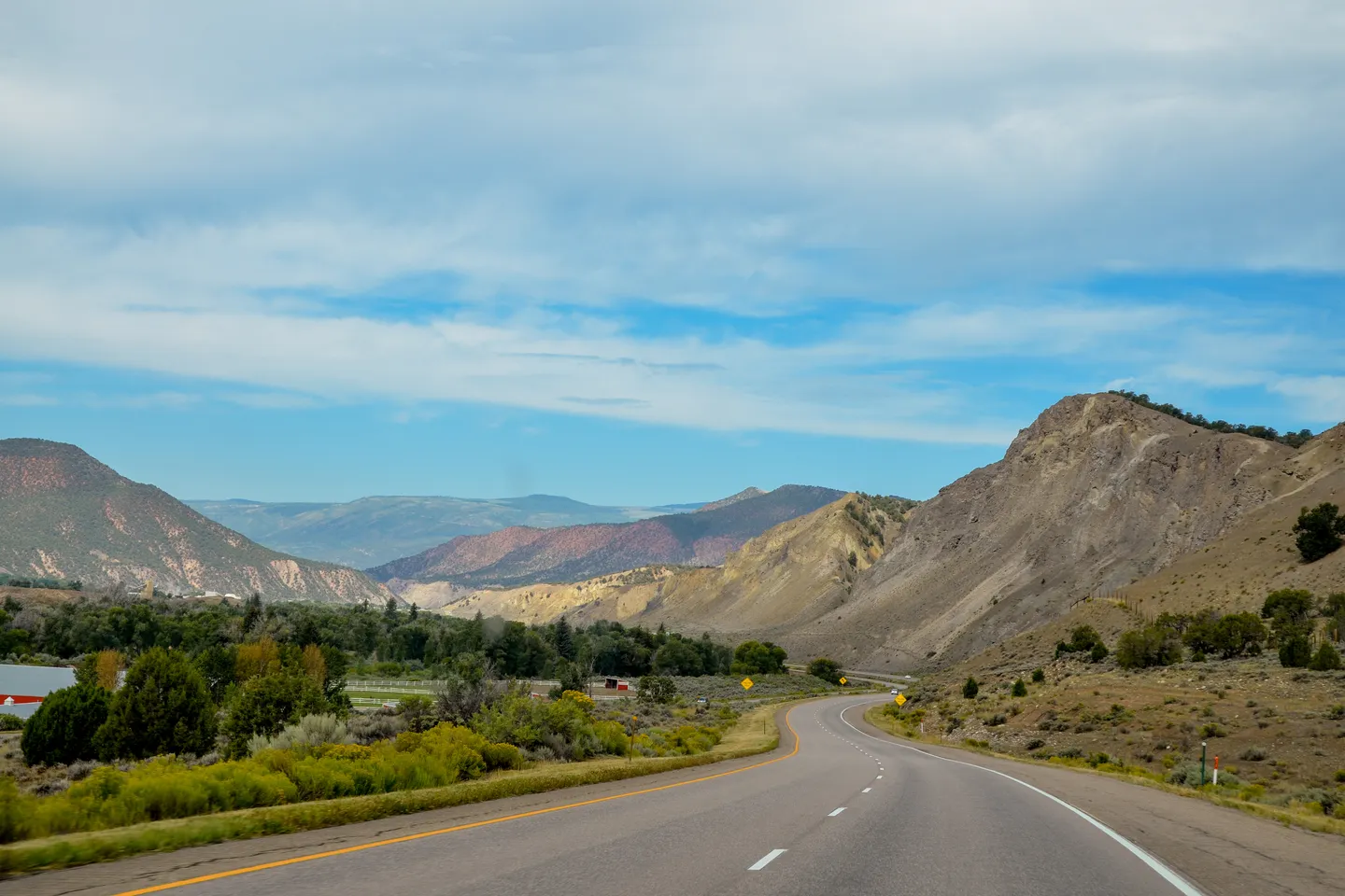 Winding highway through mountainous landscape with green vegetation and partly cloudy sky.