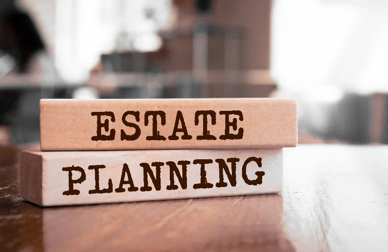 Two wooden blocks stacked on a polished surface, labeled "ESTATE" and "PLANNING" in bold brown letters.