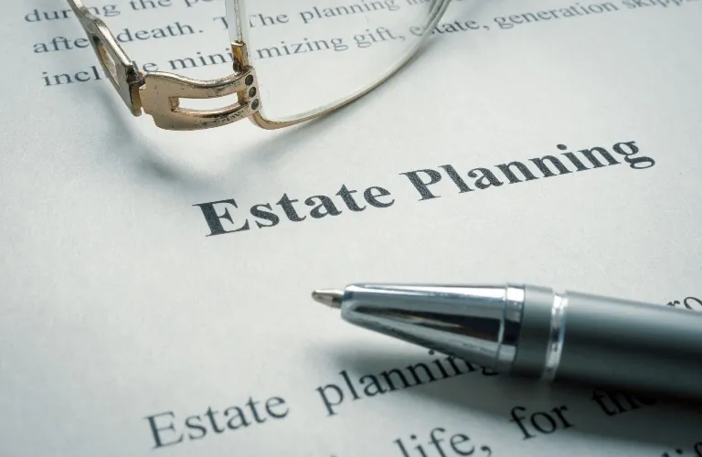 Close-up of an "Estate Planning" document with a silver pen and eyeglasses resting on the paper.