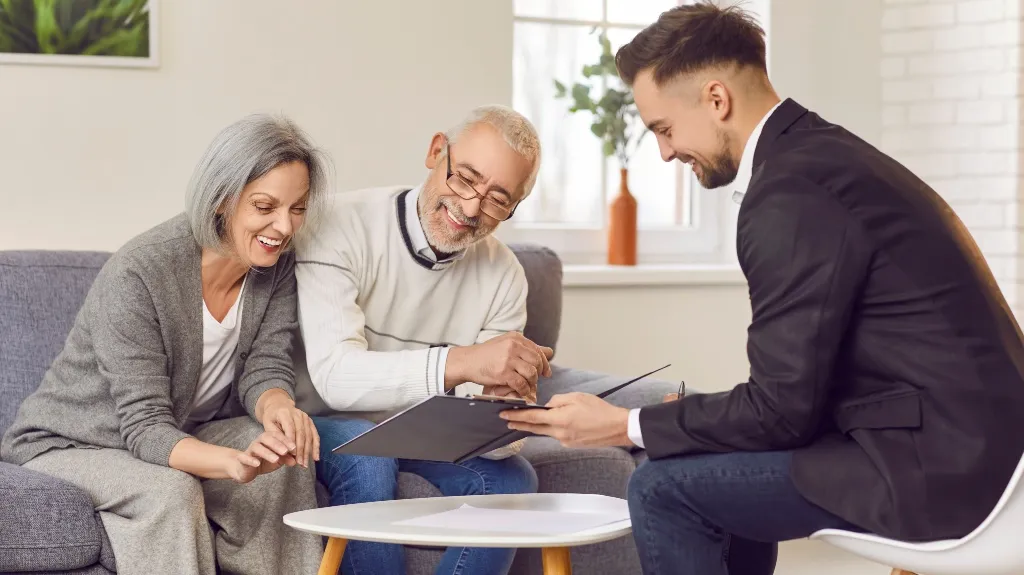 Three adults, two seniors and a younger man in business attire, reviewing documents indoors.