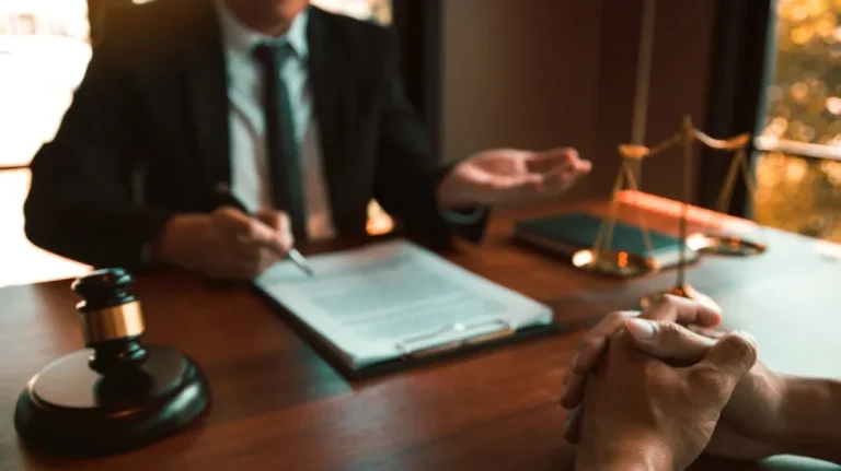 Two professionals in a legal consultation, with a gavel and scales of justice on a wooden desk.