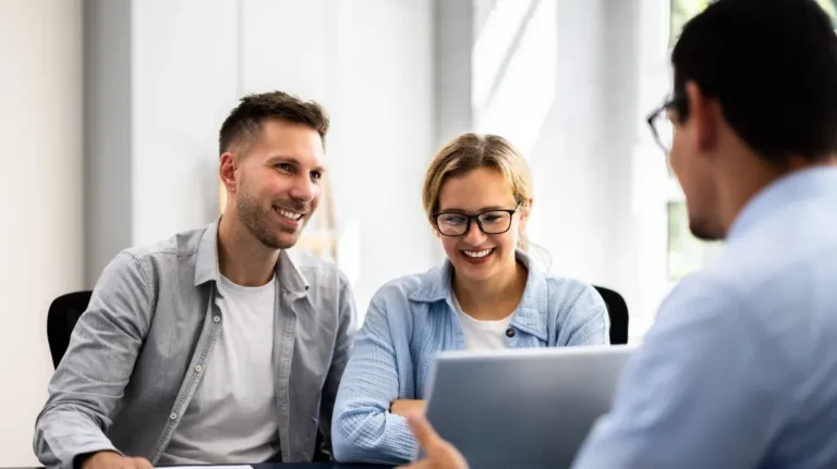 Three professionals engaged in a discussion, smiling and looking at a laptop screen.
