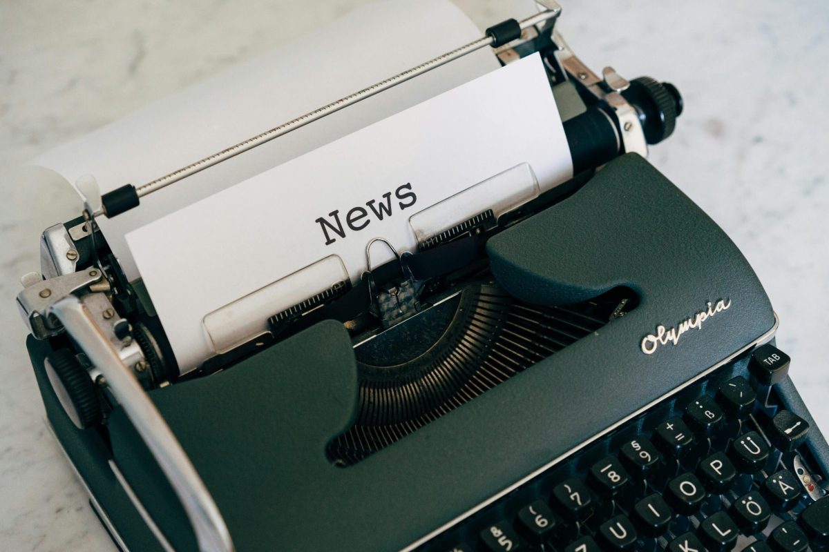 An old Olympia typewriter withe the word "News" typed in large letters on a white piece of paper.